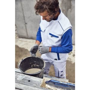 A man in a white and blue workwear softshell vest mixes material in a bucket on a construction site.