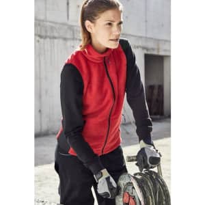 A red fleece vest worn by a woman, paired with black long sleeves and gloves, set in a work environment.