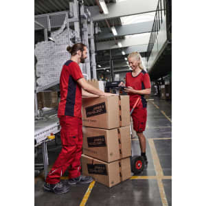 A red and black men's workwear t-shirt is worn by a man and a woman in a warehouse setting. Both are handling boxes.