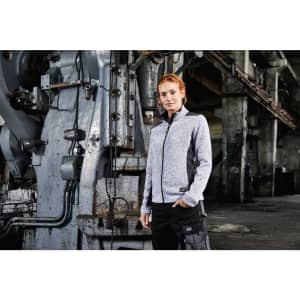 A grey ladies knitted fleece jacket with contrasting black details, worn by a model in an industrial setting.