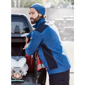 A blue knitted fleece jacket paired with a navy beanie, worn by a man leaning against a truck.
