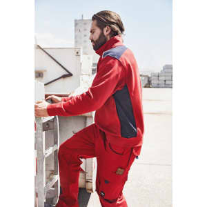A red sweat jacket with navy panels, featuring a logo, worn by a man on a worksite.