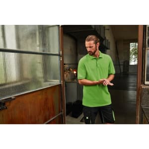 A green men's polo shirt is displayed, worn by a man standing near an industrial door. The shirt features a logo.