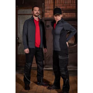 Workwear pants in black with reflective detailing, modelled by a man and a woman in red shirts and jackets.