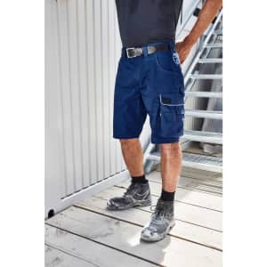 Navy workwear bermudas with multiple pockets, worn with a black belt and black shoes, standing on a wooden floor.