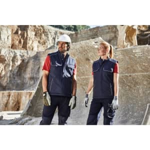 A navy blue padded work vest is worn by two individuals, one male and one female, on a worksite.