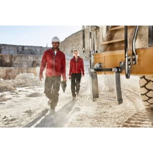 Two individuals wearing red polar fleece jackets walking in a quarry, with heavy machinery in the background.