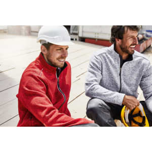 Men wearing polar fleece jackets in red and grey, sitting outdoors on a construction site. Both jackets have logos.