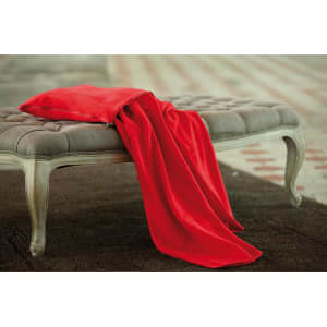 A red fleece blanket draped over a grey upholstered bench. The background features textured flooring.