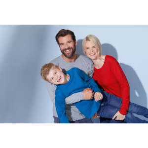 A man in a grey shirt, a woman in a red shirt, and a boy in a blue shirt, smiling together in a casual pose.