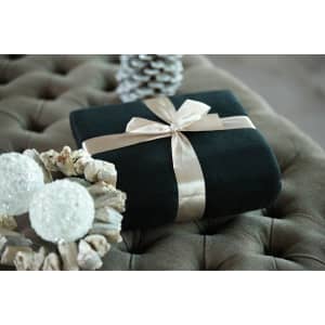 A black fleece blanket tied with a cream ribbon, placed on a tufted surface alongside decorative items.