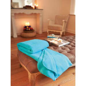 A turquoise fleece blanket draped over a brown tufted ottoman in a cozy living room setting.