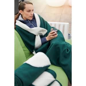 A green bonded fleece blanket with a white trim draped over a woman sitting on a couch, holding a drink.