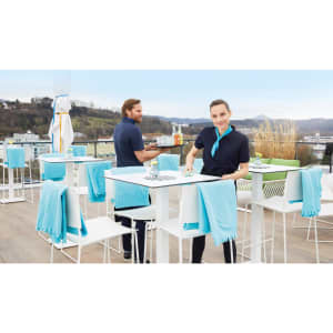 A fleece blanket in a soft blue hue drapes over white outdoor dining chairs on a balcony.