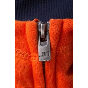 A zip on a hoodie featuring navy blue and vibrant orange fabric, with a metallic zipper and branding.