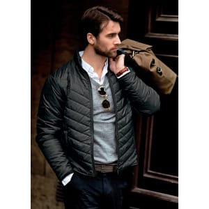 A man wearing a black quilted jacket, holding a brown bag, with sunglasses and a casual shirt underneath.