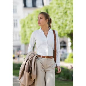 A woman wearing a white polo shirt and striped trousers, carrying a jacket and handbag, walking outdoors.