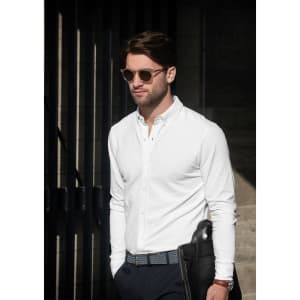 A man wearing a white long-sleeve shirt and sunglasses, holding a black bag.