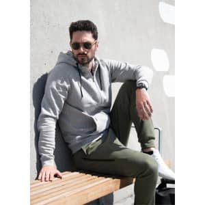 A grey hoodie jacket sits on a man lounging on a wooden bench, wearing green pants and sunglasses.