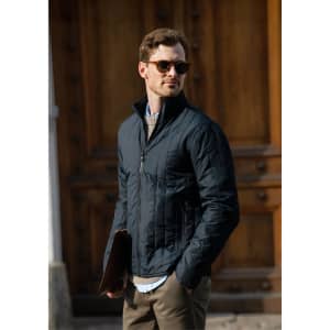 A black soft shell jacket worn by a man holding a laptop case, set against a rustic wooden backdrop.