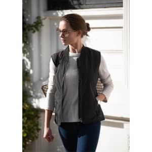 A stylish black puffer vest worn over a light top, paired with jeans, and set against a bright background.