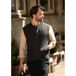 A man wearing a black vest over a light-coloured shirt, walking in an outdoor setting. The vest has a branding logo.