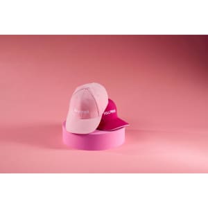 A pink and a magenta 6 Panel Sandwich Cap are displayed against a pink background, with a logo on each cap.