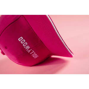 A pink 6 panel sandwich cap with a curved brim, featuring a logo on the side.
