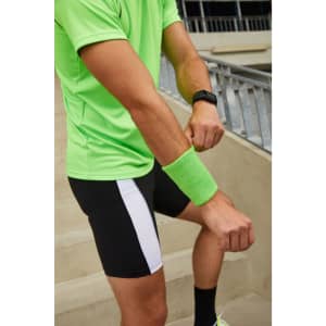 A green sporty wristband worn on the wrist of a person in a bright green shirt and black shorts.