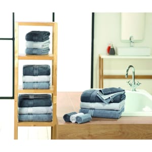 A selection of grey and white guest towels neatly folded on a wooden shelf and a countertop, with a towel set beside a bathtub.