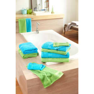 A stack of blue and green hand towels on a wooden surface near a bathtub, with more towels hanging nearby.