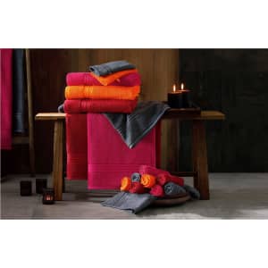 A stack of vibrant towels in pink, orange, and grey arranged on a wooden bench, with candles nearby.