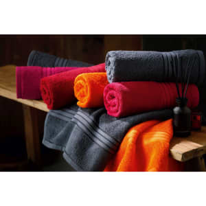 Vibrant hand towels in shades of pink, orange, and grey are neatly rolled and displayed on a wooden surface.
