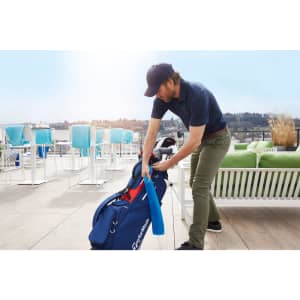 A golfer retrieves a blue golf towel from a navy golf bag, set against a sunny outdoor backdrop.