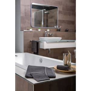 A bathroom scene featuring a white bathtub, grey towels, and a glass vase with decorative items on a wooden tray.