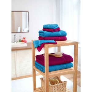 A stack of bright blue and deep red guest towels arranged on a wooden shelf, with a brush and a basket nearby.