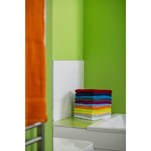 A stack of vibrant hand towels in various colours, neatly arranged against a green wall in a bathroom setting.