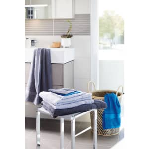 A collection of flannel hand towels in grey and blue, neatly arranged on a metal stool beside a woven basket.