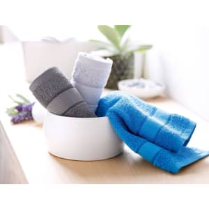 Hand towels in shades of grey, blue, and light blue arranged in a white bowl on a wooden surface. A plant is visible in the background.