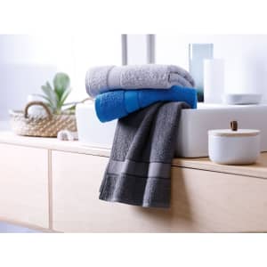 Three hand towels in shades of grey, blue, and light grey are neatly folded on a wooden surface with decorative items.
