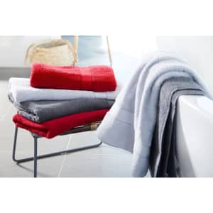 A stack of bath towels in red, grey, and white, arranged neatly on a metal stand beside a bathtub.