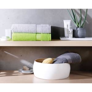A set of grey and green bath towels stacked neatly beside a potted plant and various toiletries on a wooden surface.