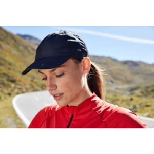 A navy 6 Panel Coolmax® Cap worn by a woman in a red top, with a blurred mountain road in the background.