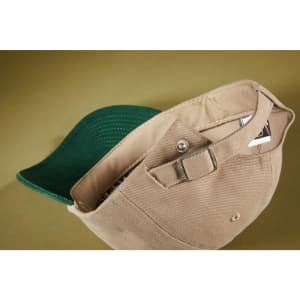 A beige 6 panel cap with a green peak, featuring an adjustable strap and a logo inside.