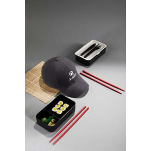 A brushed black cap with a logo, arranged alongside a sushi bento box, chopsticks, and utensils.