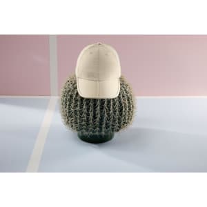 A beige cap rests on a green cactus, set against a pink and blue backdrop. The cap features a logo.