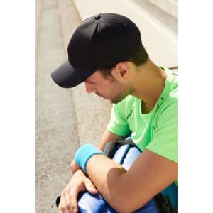 A black 6-panel sport mesh cap worn by a man in a bright green shirt, sitting with a blue bag on his lap.