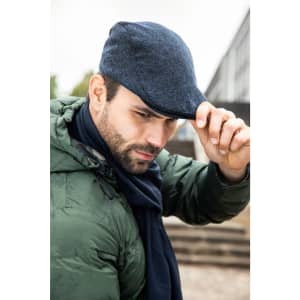 A man wearing a dark blue cap and a green jacket, adjusting his cap with a serious expression.
