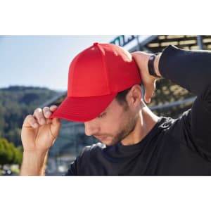 A red 6 panel sports cap on a man wearing a black long-sleeve shirt, with a logo on the cap.