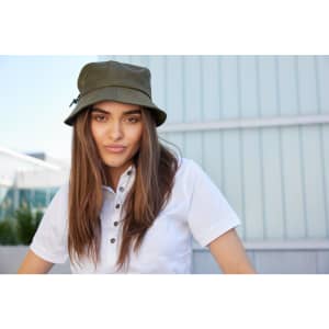 A woman wearing an olive green fisherman hat, with long hair, set against a modern building backdrop.